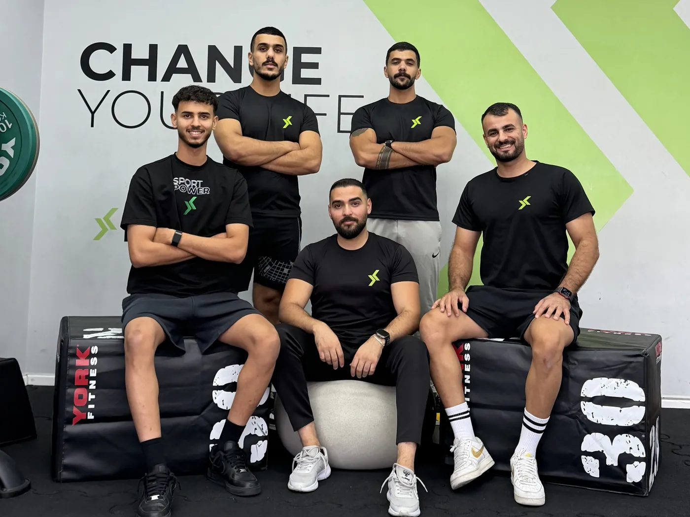 The Sport Power coaching team in front of the CHANGE YOUR LIFE wall